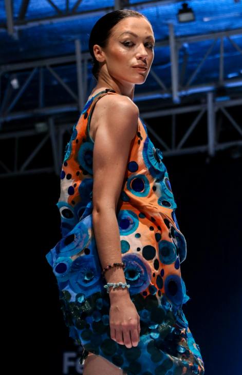 A model walking down the runway wearing a colorful dress with blue and orange patterns during a fashion show.